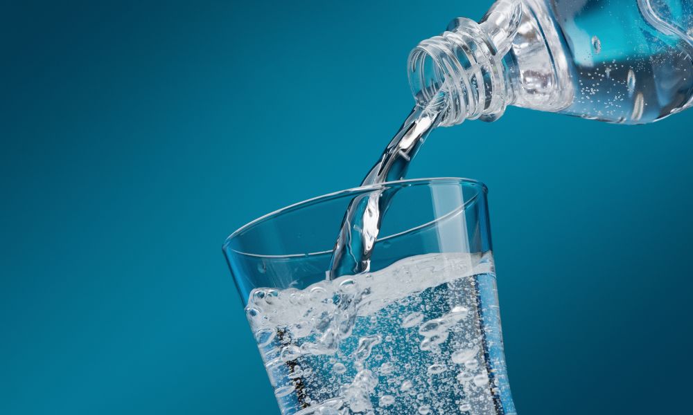 Water bottle pouring water into a glass cup that is almost all the way full and about to overflow 